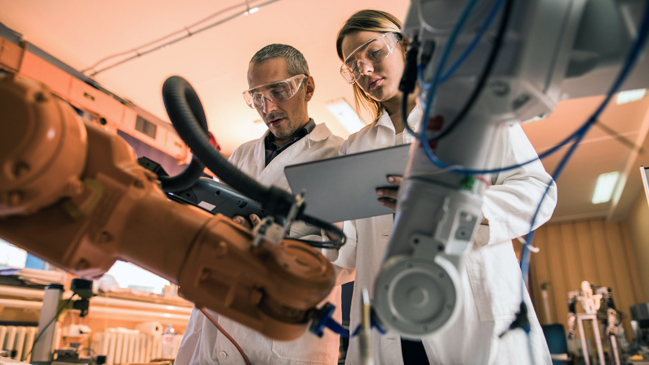 Low angle view of two engineers working on robotic arm in laboratory. Woman is using digital tablet.