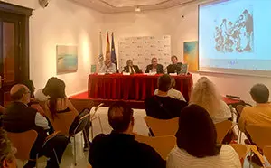 3. La mesa con los intervinientes, parte del público y la pantalla en la que se proyectó un juego típico de la época que describe el libro