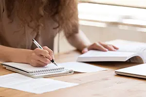 Close up of female student sit at table study using  handbook write in notebook doing research, motivated girl prepare for test or exam learning handwriting in workbook, making notes of important data