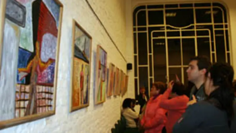  Un grupo de asistentes observan las pinturas de la muestra.