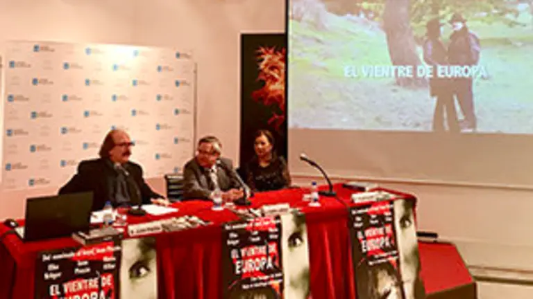 2. En la mesa, de izquierda a derecha, el director Juan Pinzás, el coordinador de Actos  Ramón Jiménez y la productora Pilar Sueiro con una imagen del trailes de la película EL VIENTRE DE EUROPA.jpg 