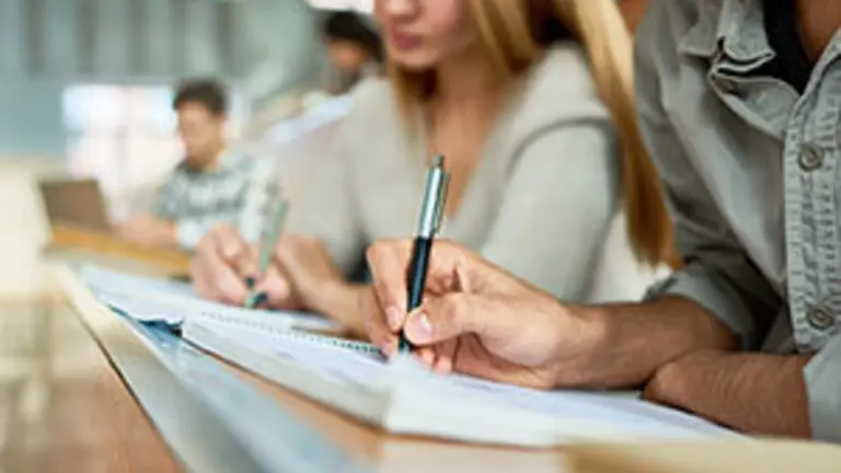 Close up of male student taking notes sitting at desk during lecture in college, focus on hand writing in notebook, copy space