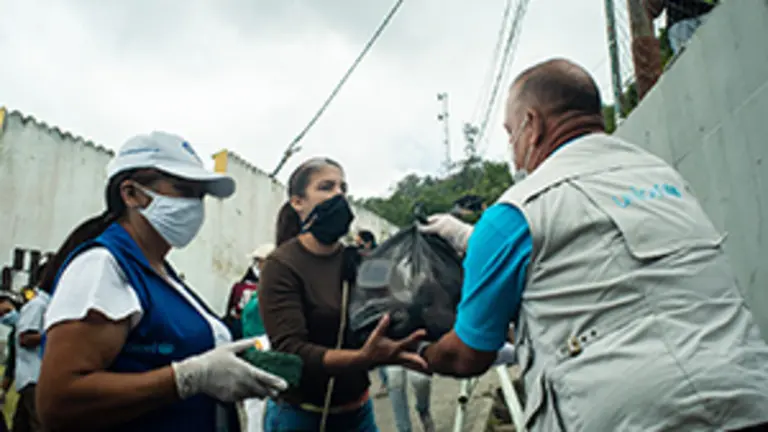 UNICEF staff gives a woman the food kit delivered by UNICEF on the outskirts of Caracas, Venezuela on April 29, 2020.

The deteriorating situation inside Venezuela puts children at risk of dropout school. Since 2019, UNICEF started a pilot program to support school feeding program in prioritized educational centers to prevent the drop out school. In order to keep the access to school feeding service during quarantine due to COVID-19, UNICEF has provided food kits to the students family instead.

