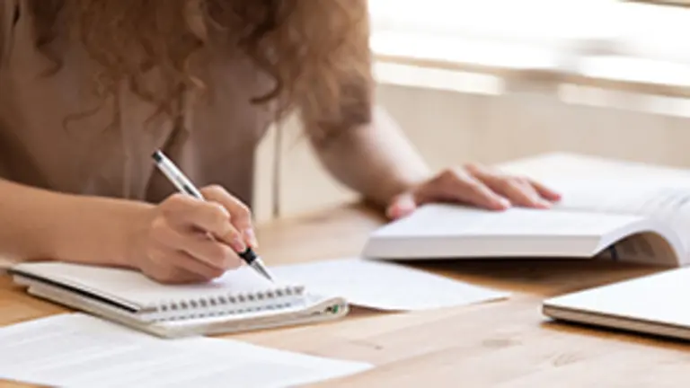 Close up of female student sit at table study using  handbook write in notebook doing research, motivated girl prepare for test or exam learning handwriting in workbook, making notes of important data