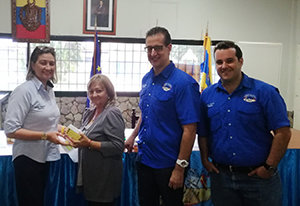 La secretaria general del CCEC hace entrega de medicamentos a una de las beneficiarias en presencia del presidente y vicepresidente de la entidad.